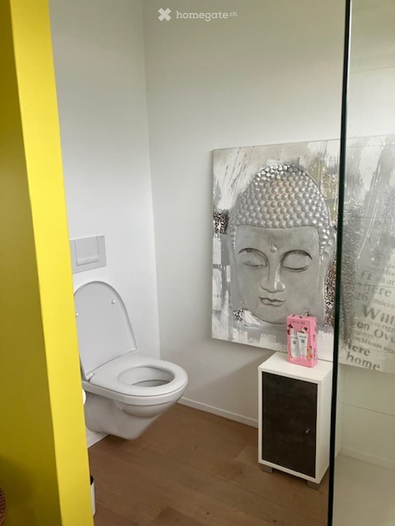 Modern bathroom with white toilet, small white cabinet, and a large Buddha head picture on the wall.