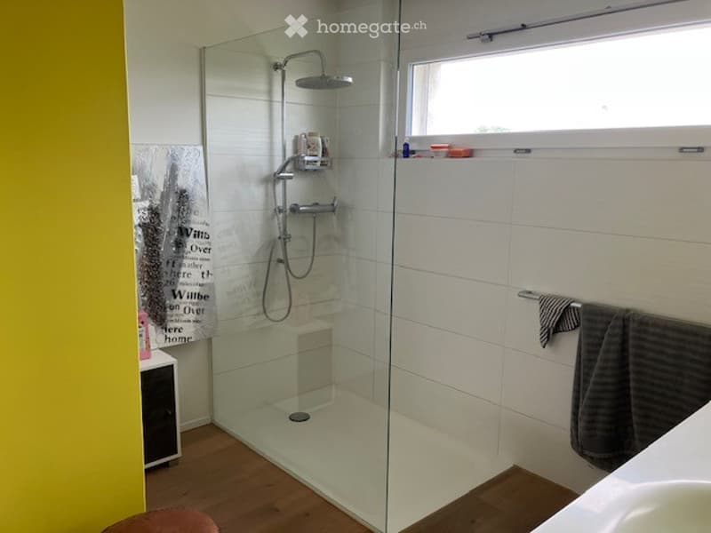Modern bathroom with a glass-enclosed shower stall, a showerhead, a towel hanging on the wall, a sink, and a cup on the windowsill.