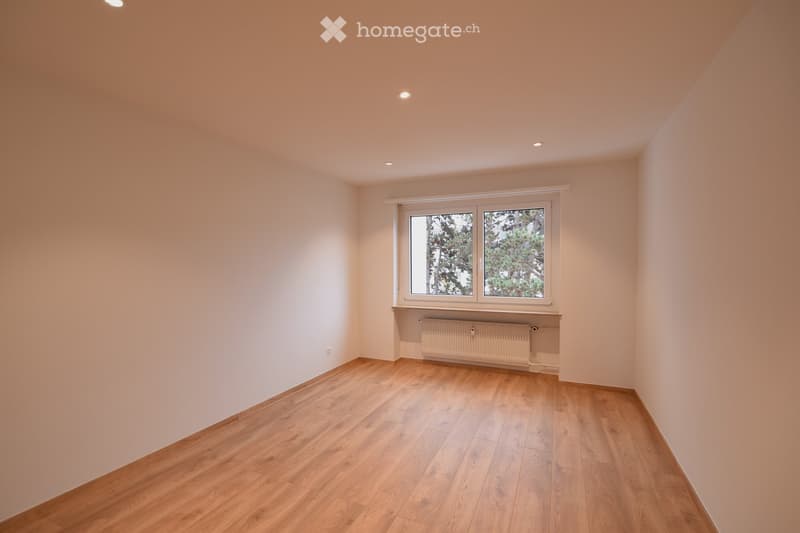 Empty room with wooden flooring, white walls, and a large window with a radiator below it.