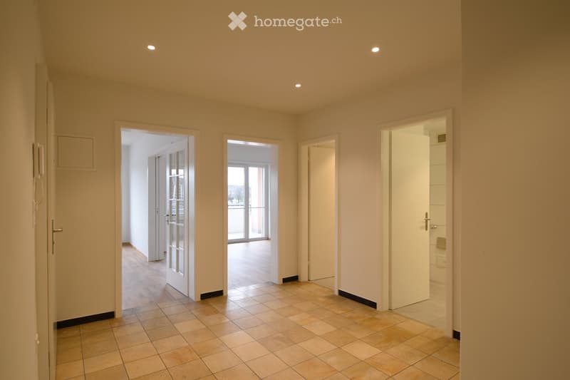 Empty hallway with tiled floor, several doors leading to other rooms, and recessed ceiling lighting.