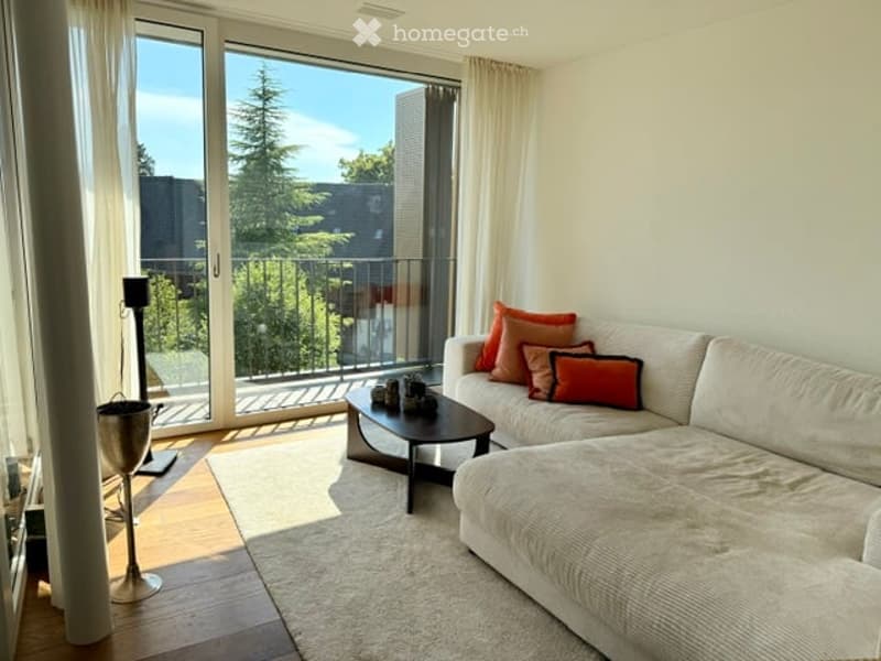 Modern living room with large windows and balcony access, featuring a white sectional sofa with colorful throw pillows, a black coffee table, a floor lamp, and a white area rug.