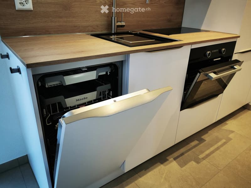 Modern kitchen with wooden countertops, stainless steel sink, dishwasher, and oven. White cabinets and sleek design.