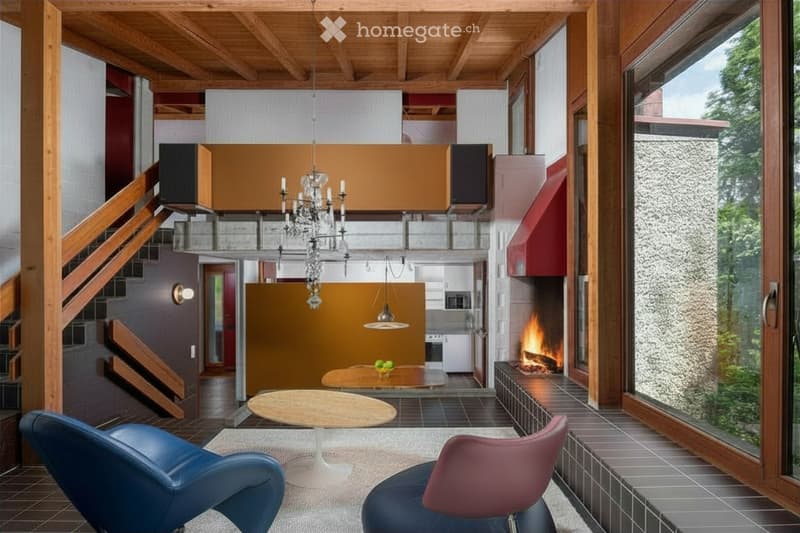 Modern living room with exposed wooden beams, fireplace, large windows, and contemporary furniture including a sofa, table, and chairs.