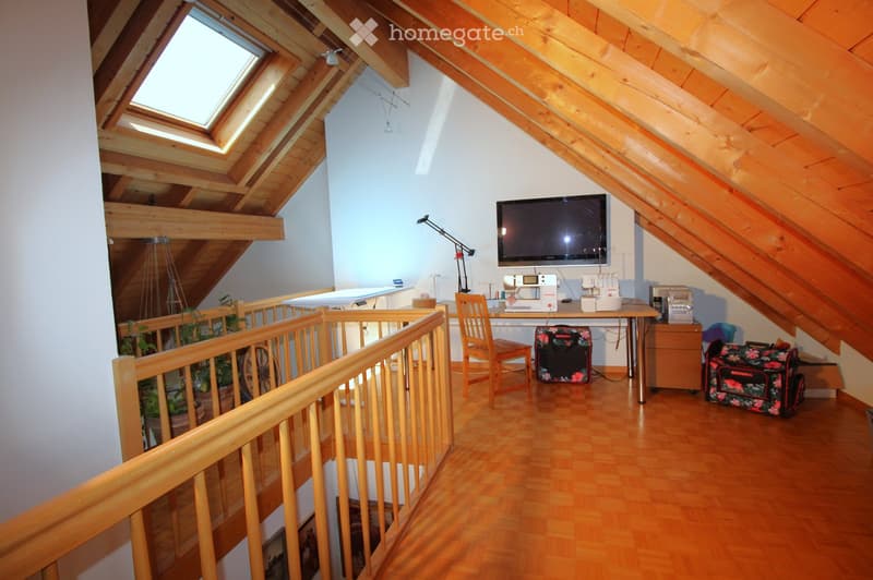Attic room with wooden beams, skylight windows, wooden floor, and a desk area with a sewing machine, chair, and television mounted on the wall.