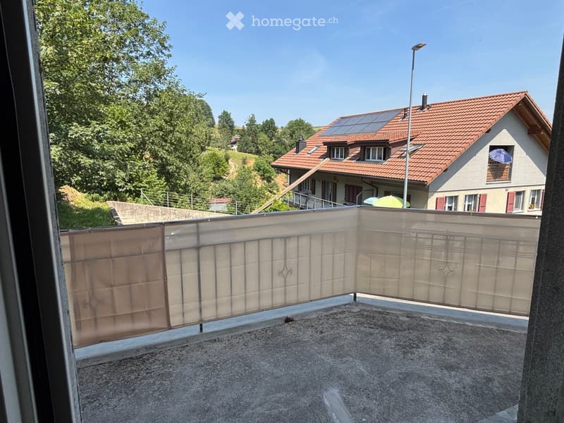 Balcony with metal railing, concrete floor, and view of a house with red-tiled roof and solar panels.