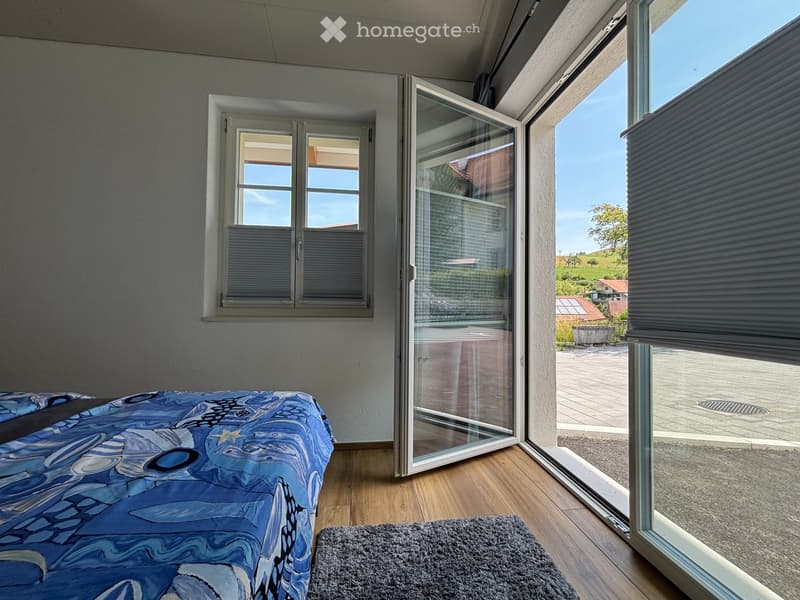Bright bedroom with wooden flooring, large windows, and a bed with a blue patterned duvet.