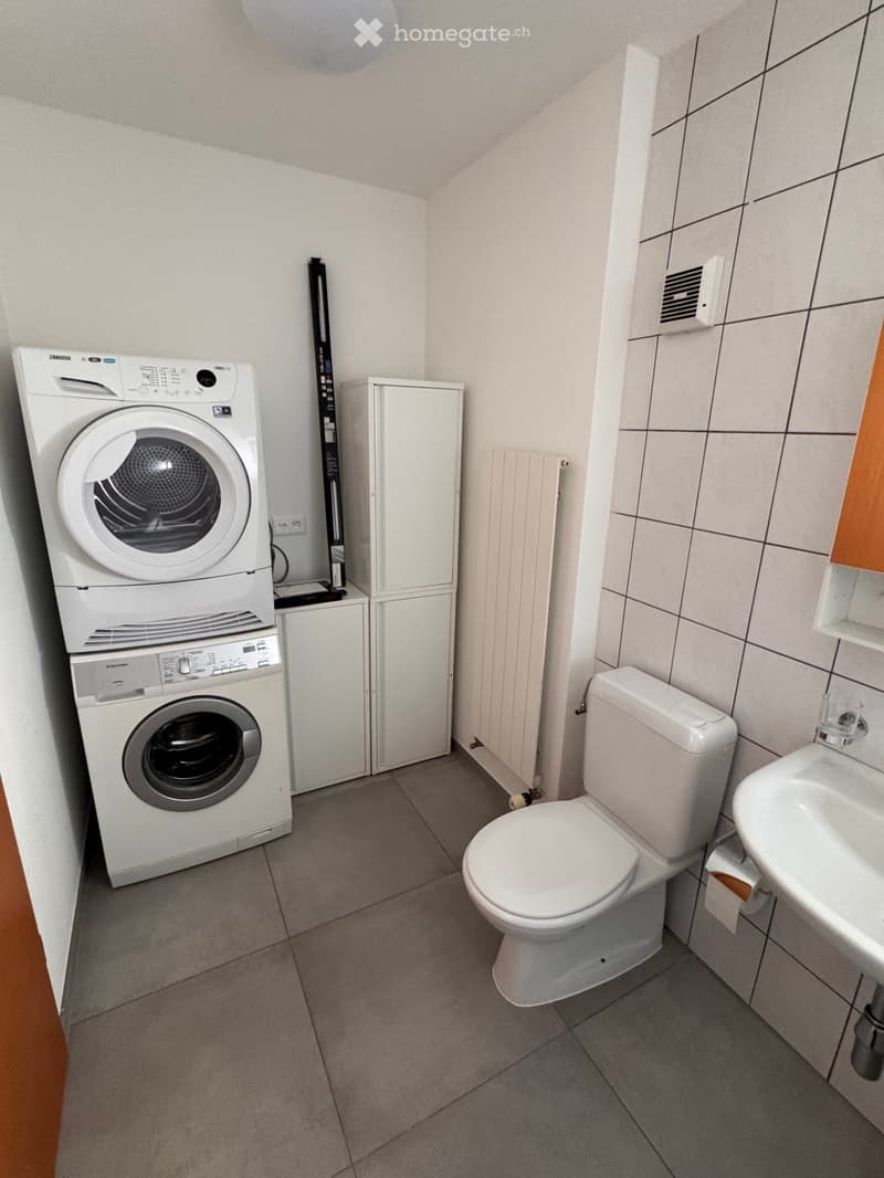 Modern bathroom with a toilet, sink, and stacked washing machine and dryer unit.
