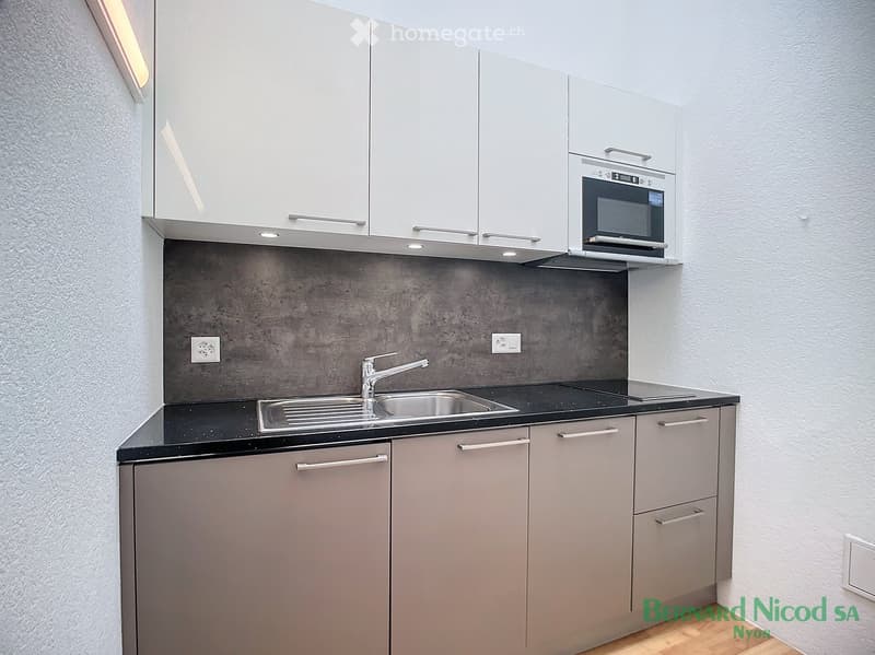 Modern kitchen with gray cabinets, black countertop, built-in oven, and a stainless steel sink with faucet