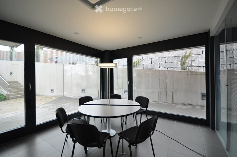 circular white table, 6 black chairs, table lamp, concrete floor, glass walls, exterior view