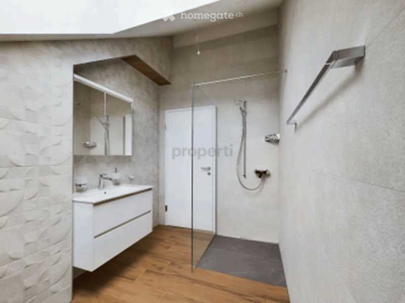 Modern bathroom with a white vanity, sink, mirror, and a glass-enclosed shower area. The walls are tiled, and the floor is wooden.