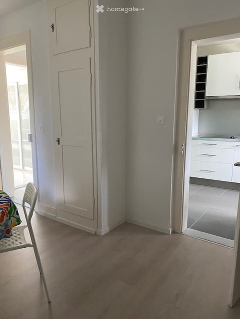 empty room, wooden floor, white walls, white doors, table and chair, kitchen area