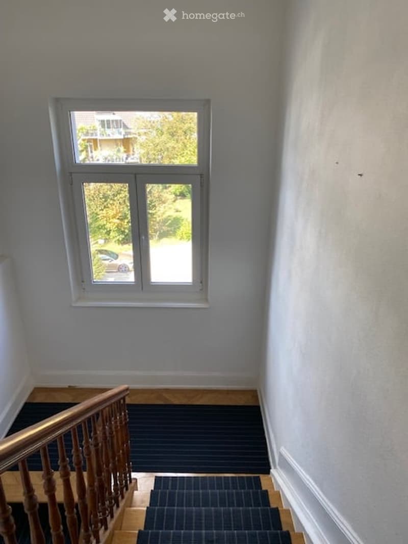 white walls, wooden handrail, white window, tiled floor, striped black carpet on stairs