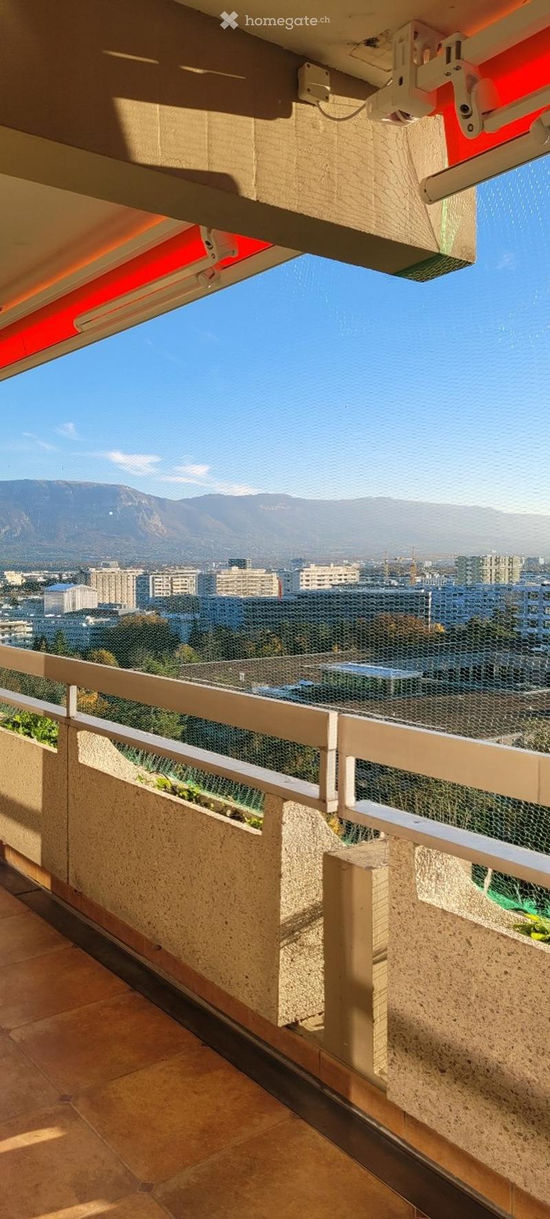 Balcony with tiled floor, white railing, and a panoramic view of a cityscape and mountains.