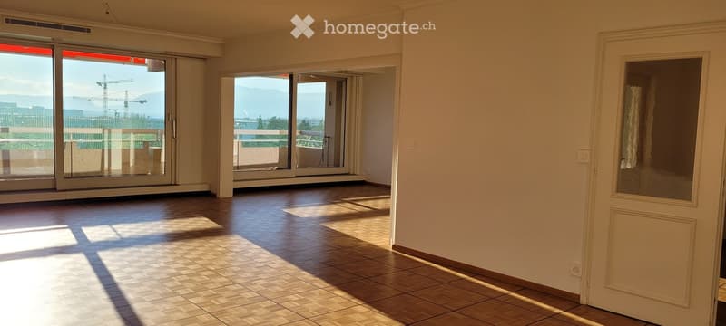 Empty room with wooden flooring, large sliding glass doors leading to a balcony with a scenic view of mountains and a construction site.
