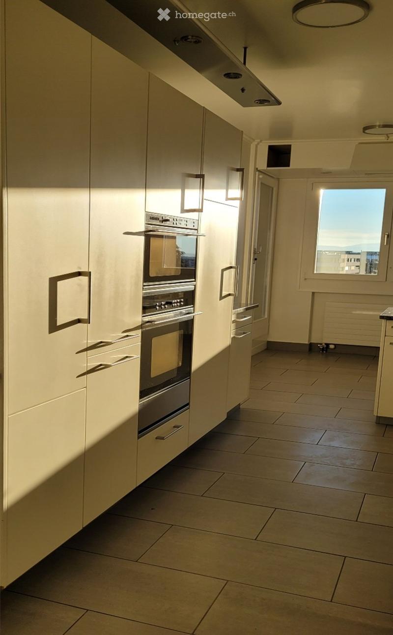 Modern kitchen with light-colored cabinets, built-in oven, tiled floor, and large window providing natural light.
