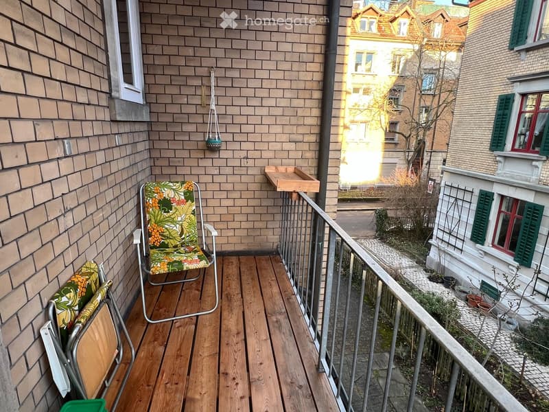Balcony with wooden decking, metal railing, and a single chair with a colorful cushion.