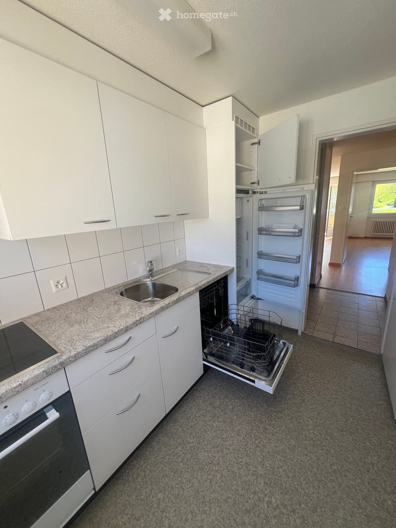 Modern kitchen with white cabinets, granite countertop, stainless steel sink, oven, dishwasher, and refrigerator. Open shelving is visible in the background.