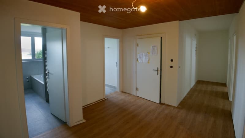 Empty hallway with wooden flooring, white walls, and several doors leading to different rooms.