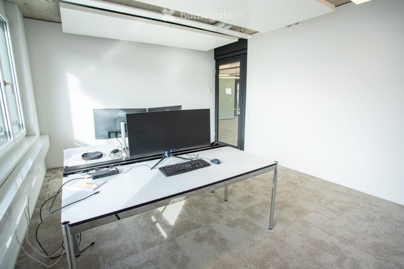 Modern office space with a white desk, multiple computer monitors, keyboard, mouse, laptop, and various office supplies.