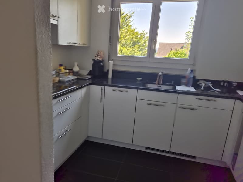 Modern kitchen with white cabinets, black countertops, and stainless steel appliances. Features a sink, faucet, and various kitchen items on the counter.