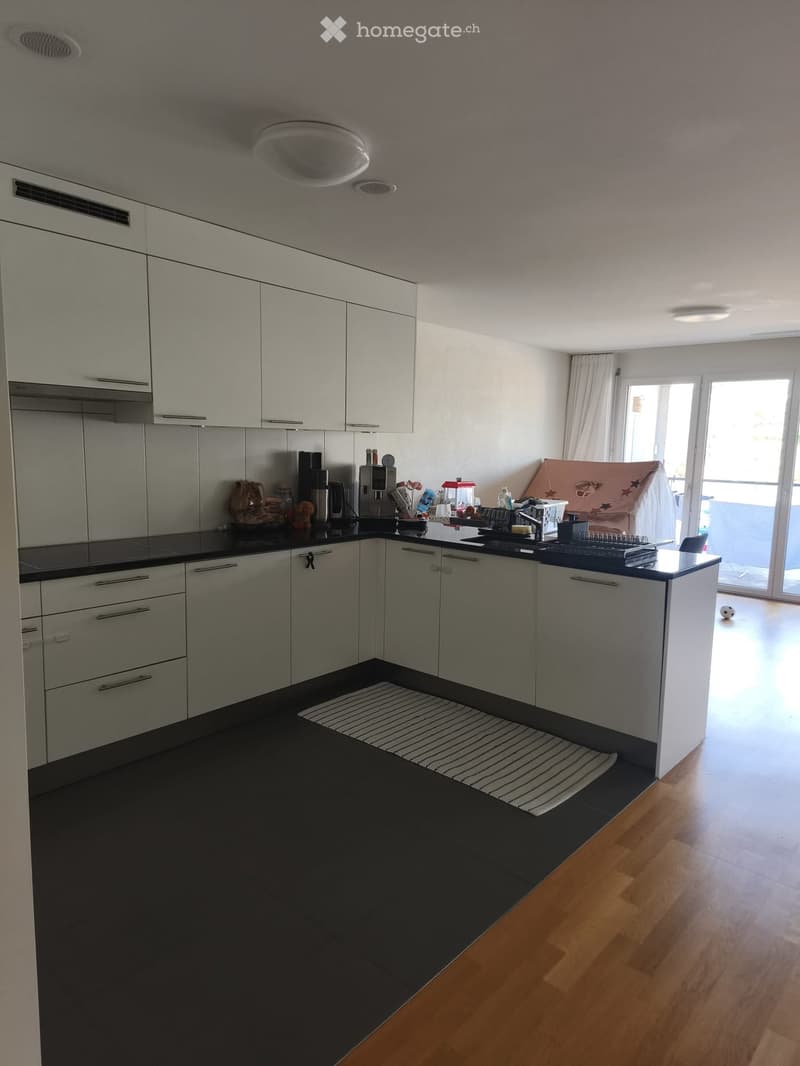 Modern kitchen with white cabinets, black countertops, and a small island. Coffee maker, sink, and dish rack are visible.