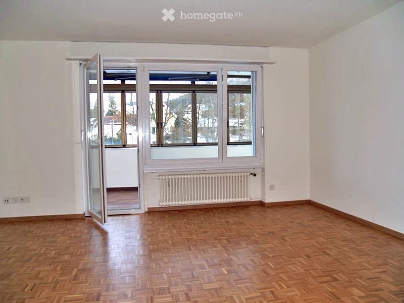 Empty room with wooden flooring, white walls, large windows, and a radiator. No furniture or equipment present.