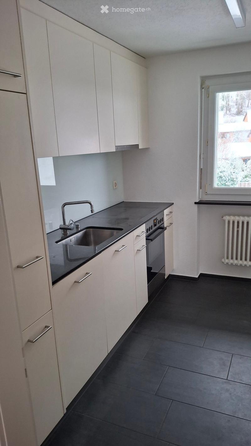 Modern kitchen with white cabinets, black countertops, stainless steel sink, and built-in oven. Features a window and radiator.