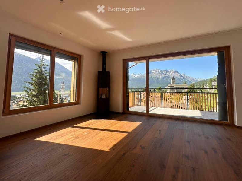 Bright, empty room with wooden flooring and large windows offering scenic mountain views. Features a sliding glass door leading to a balcony.