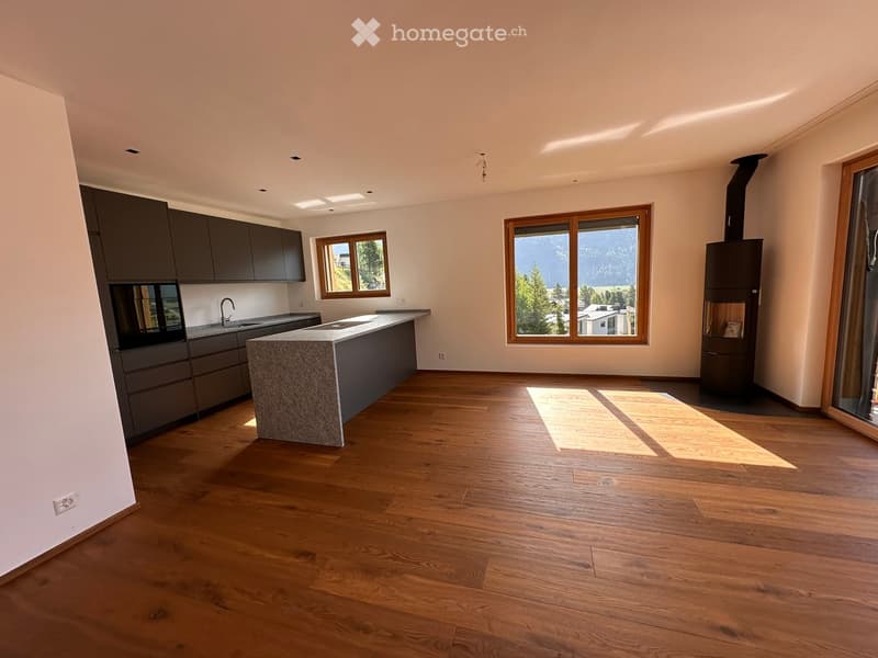 Modern kitchen with wooden flooring, large island, dark cabinets, and a wood-burning stove. Large windows offer a scenic mountain view.