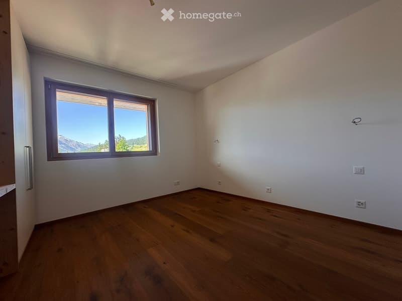 Empty room with wooden flooring, white walls, and large windows offering a scenic mountain view.