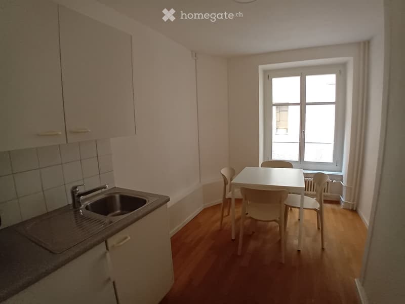 A small kitchen and dining area with light wooden flooring, white cabinets, a sink, and a small dining table with chairs.