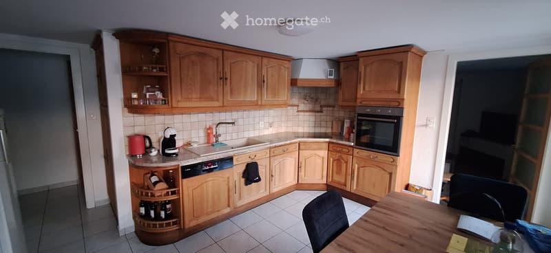 A well-equipped kitchen with wooden cabinets, a sink, an oven, a dishwasher, a coffee maker, and a wine rack. The space includes a dining area with a wooden table and chairs.
