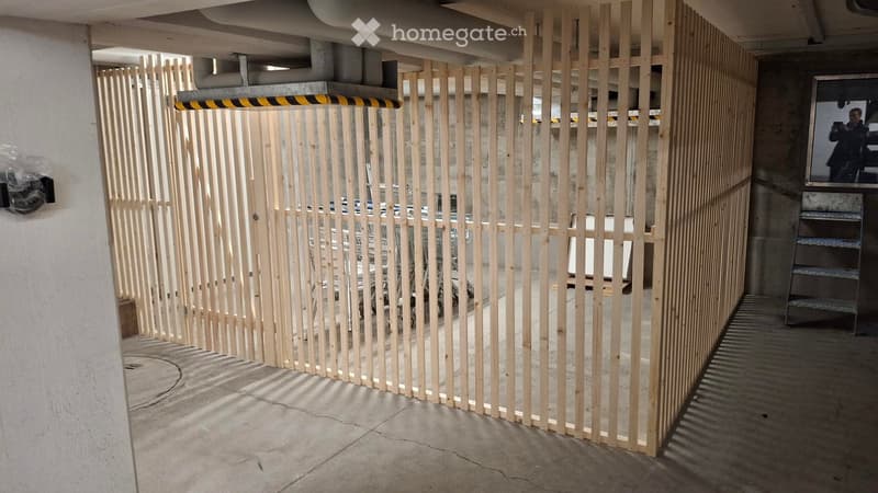 A modern, minimalist hallway with a wooden slatted partition, concrete walls, and a metal staircase leading upwards.