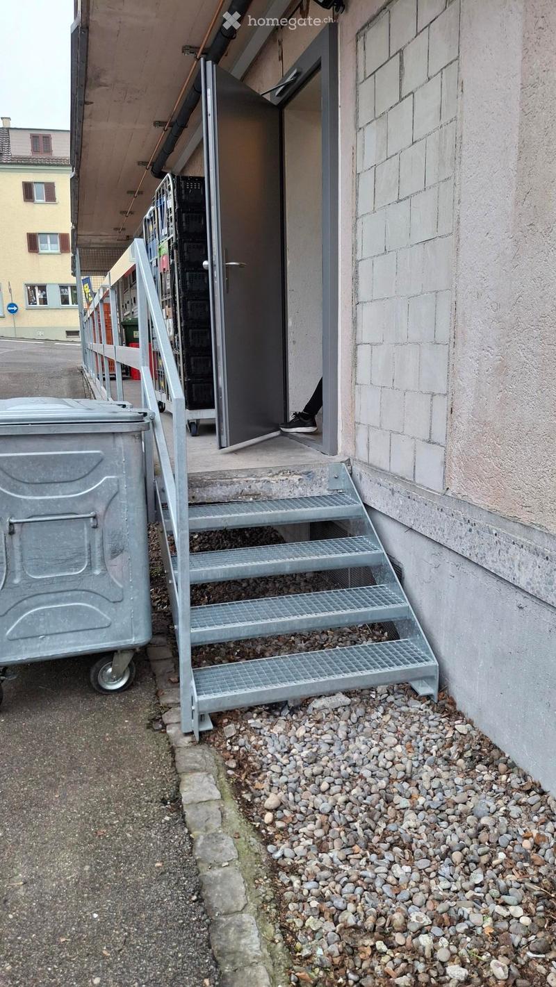 Metal staircase leading to a doorway, with a metal railing and a gravel pathway.