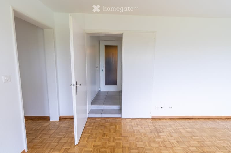 Empty hallway with wooden flooring, white walls, and open doors leading to other rooms.