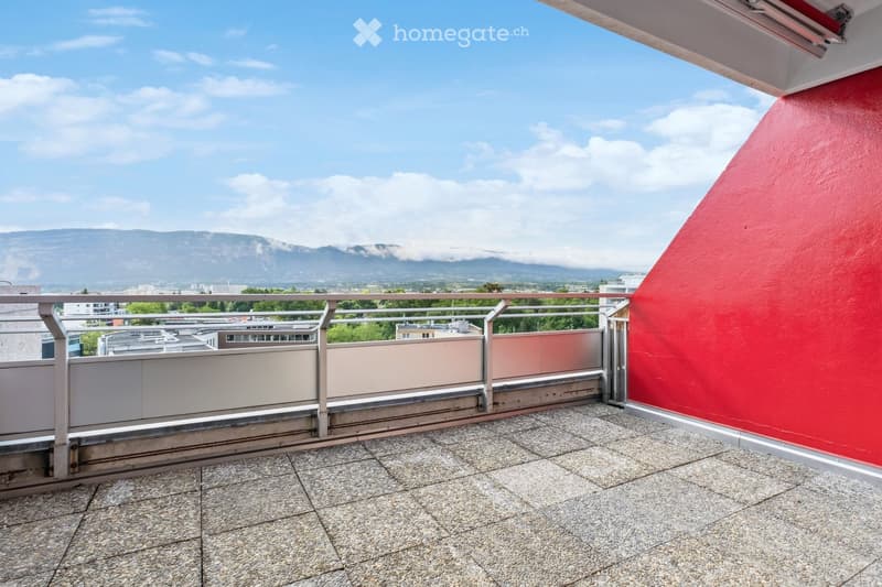 Balcony with tiled floor, metal railing, red wall, and scenic mountain view.