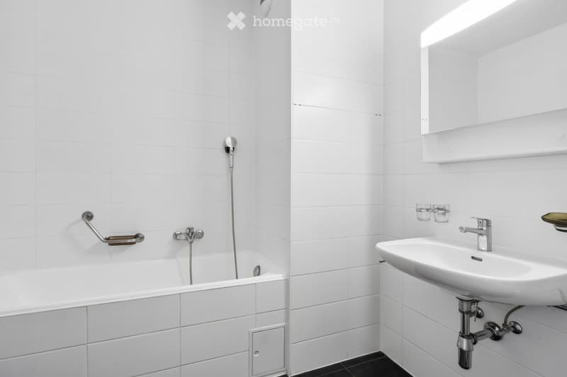 Modern bathroom with white tiled walls, a bathtub with a handheld shower, a sink with a modern faucet, and a mirror above the sink.