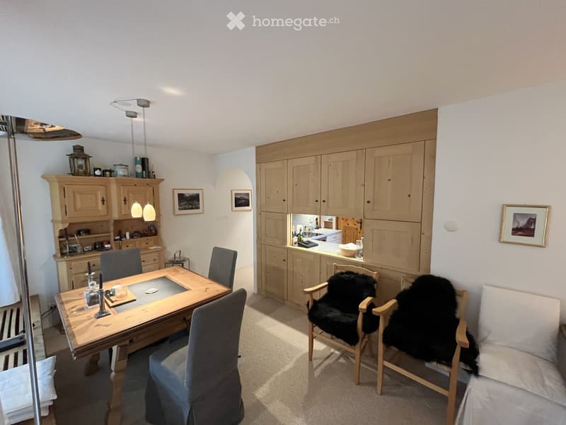 A cozy, well-lit dining and living area with a wooden dining table, chairs, a sofa, and built-in wooden cabinets.