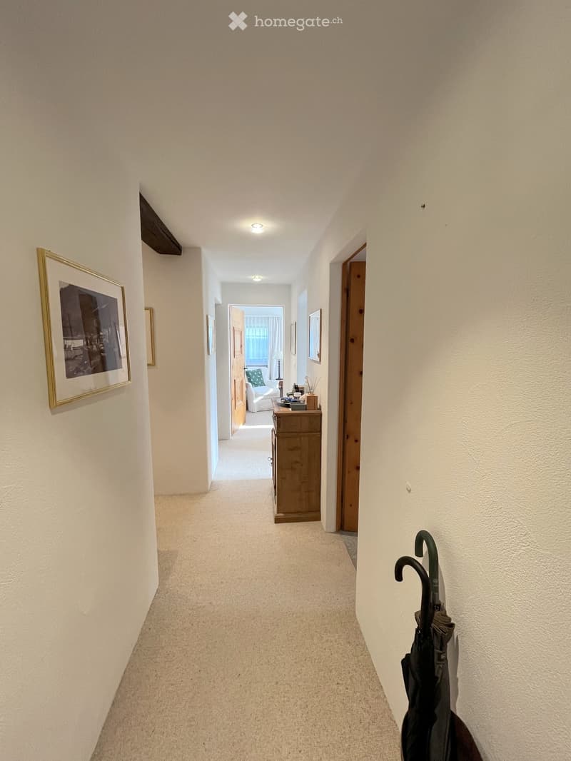 Carpeted hallway with white walls, recessed lighting, framed artwork, and a small console table with items on it at the end.