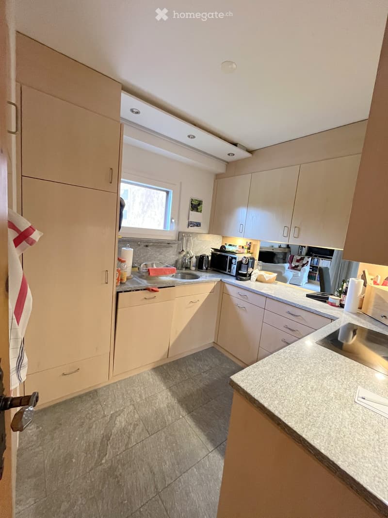 Modern kitchen with light-colored cabinets, granite countertops, and stainless steel appliances including a microwave and coffee maker. Features a window above the sink and a tiled floor.