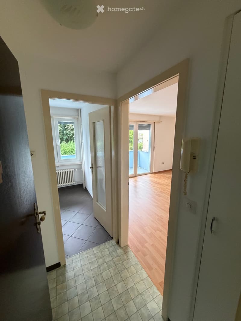 Hallway with tiled floor, leading to rooms with wooden flooring and large windows, featuring a radiator and intercom system.