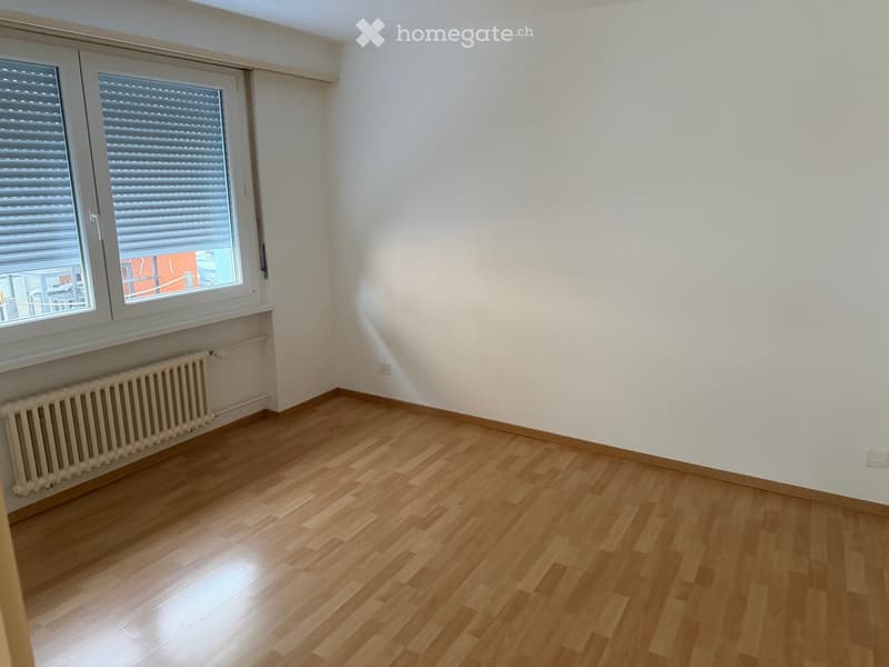 Empty room with wooden flooring, white walls, and large windows with blinds. A radiator is visible under the windows.