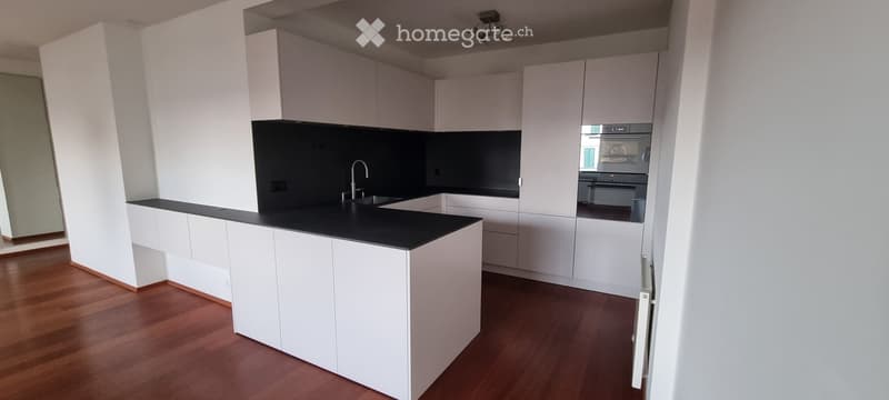Modern kitchen with white cabinets, black countertops, and wooden flooring.