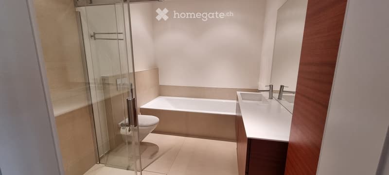 Modern bathroom with a bathtub, toilet, double sink, and a glass-enclosed shower area.