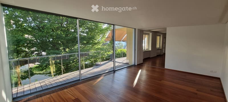 Empty room with wooden flooring, large glass sliding doors leading to a balcony, and natural light from the windows.