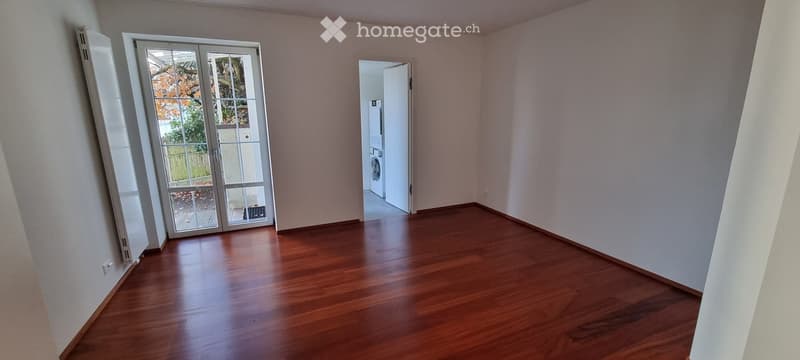 Empty room with wooden flooring, white walls, and a large sliding glass door leading to a balcony.