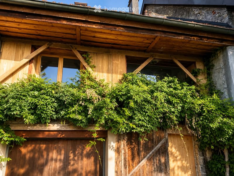 Wooden building facade with ivy-covered sections, wooden shutters, and a stone wall on the right side.