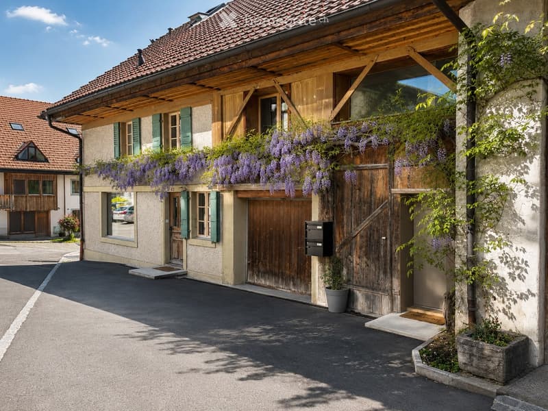 Traditional two-story building with wooden shutters, tiled roof, and purple wisteria climbing on the facade. Features a wooden garage door, small potted plant, and a mailbox.