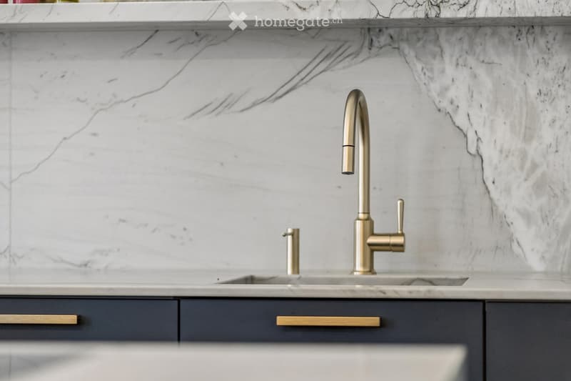 Modern kitchen sink area with a sleek gold faucet, marble countertop, and dark grey cabinets.