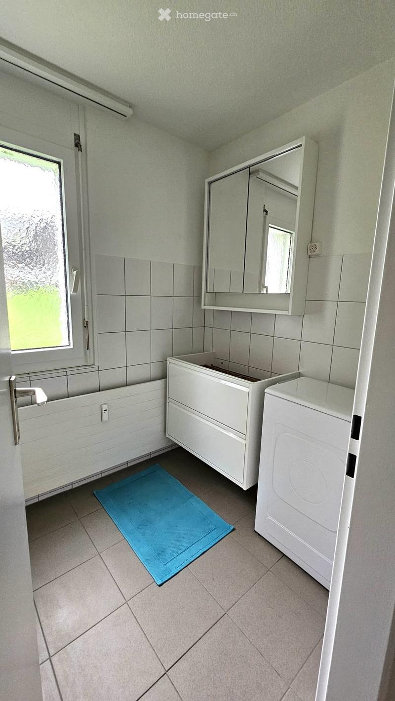 Bathroom with a bathtub, sink, mirror cabinet, washing machine, and a blue bath mat on the floor.